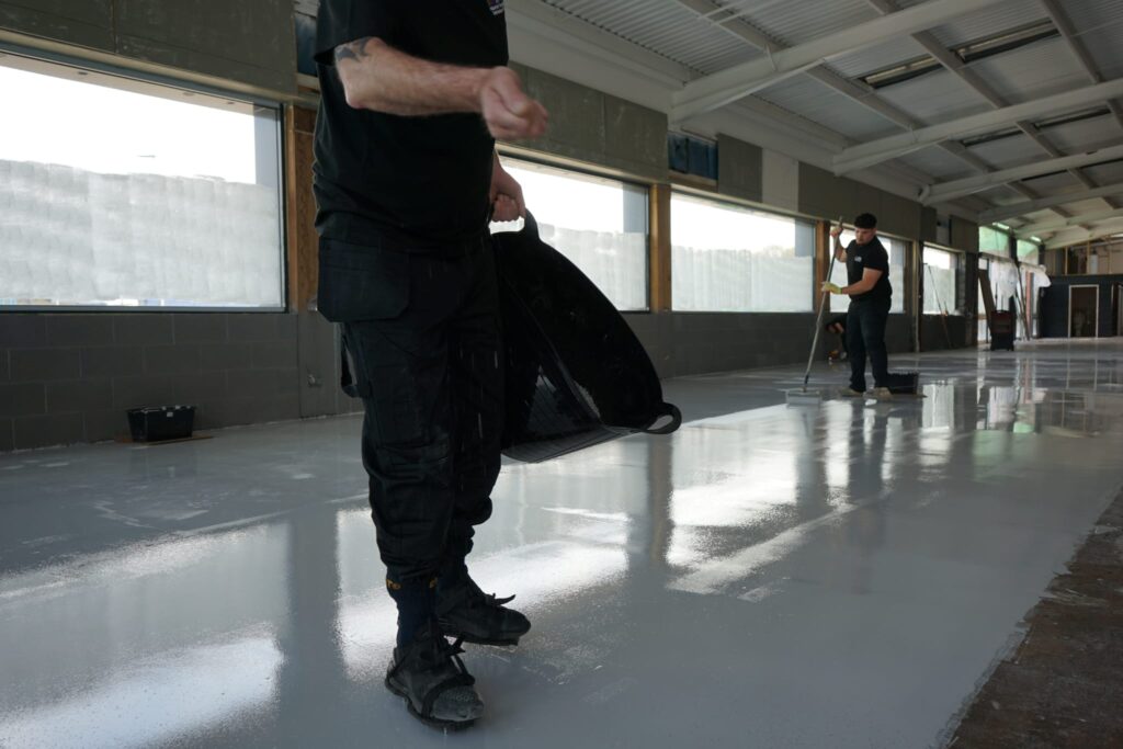 Lee Taylor broadcasting decorative flakes by hand over self levelling epoxy resin floor wearing spike shoes in West Bromwich commercial space