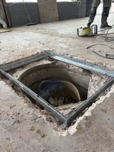 Setting manhole frame in place during self levelling epoxy resin floor installation in West Bromwich commercial space