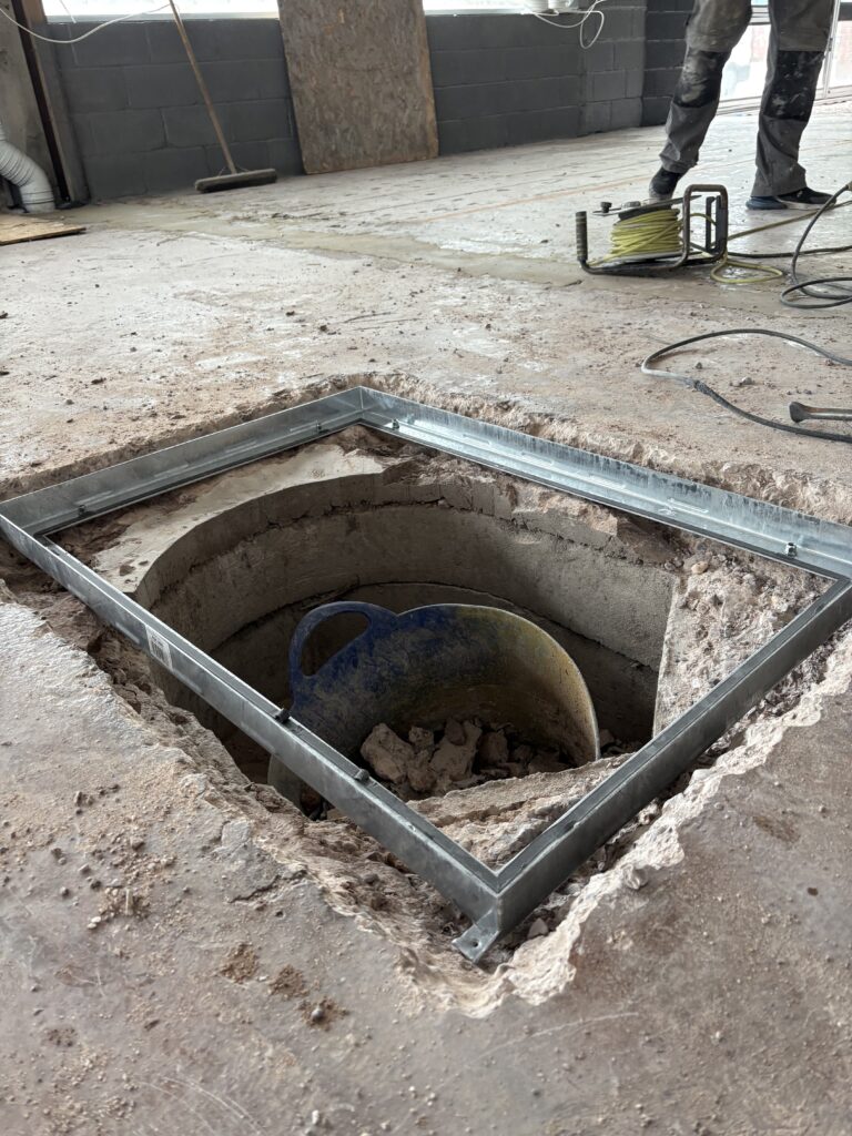 Setting manhole frame in place during self levelling epoxy resin floor installation in West Bromwich commercial space